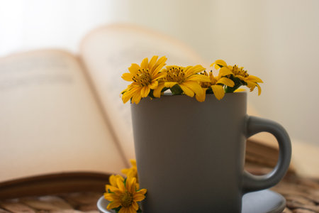 A cup of coffee with yellow flowers and open book on the tableの写真素材