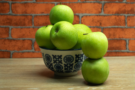 Green apples in a bowl on a wooden table with brick wall background