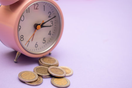 Pink alarm clock and coins on purple background. Time is money concept.