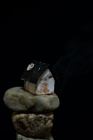 house on a pile of stones with smoke on a black background.の写真素材