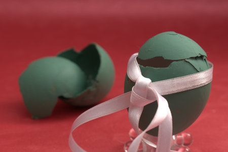 Broken green easter egg with a ribbon on a red background