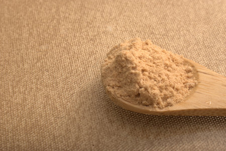 Powdered brown sugar in wooden spoon on sackcloth background
