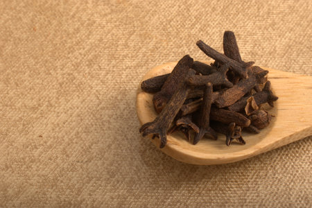 Cloves in a wooden spoon on sackcloth background, close upの写真素材