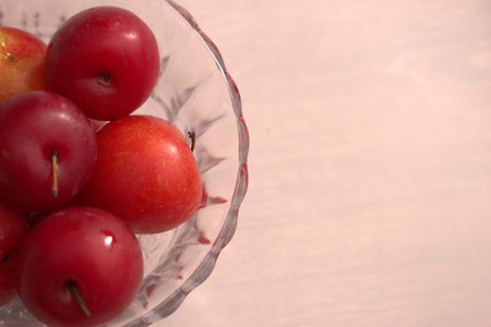 Fresh red plums in a glass vase on a white wooden backgroundの写真素材