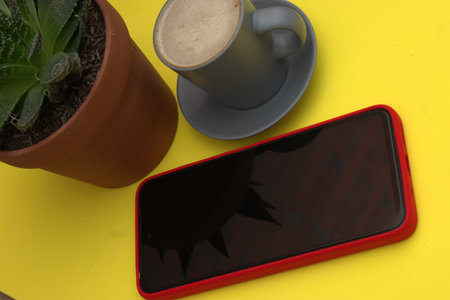 Smartphone and coffee cup on yellow background. View from above.の写真素材