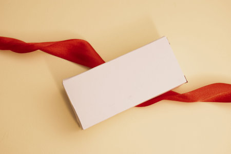 White gift box with red ribbon on beige background. Close up.の写真素材