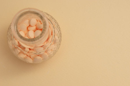 Close-up of pills in glass jar on beige background.