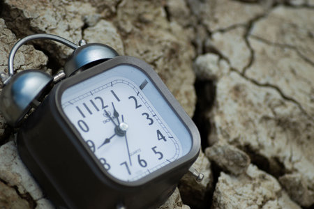 Alarm clock on the background of dry soil. Time concept.の写真素材