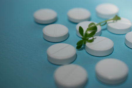 Close up of white pills and green plant on blue background with copy spaceの写真素材