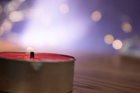 Red candle on wooden table in front of bokeh background.