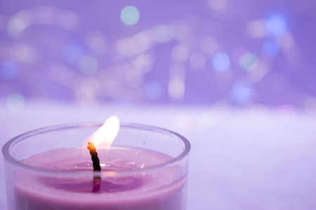 Candle on purple background with bokeh effect. Selective focus.