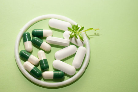 Green and white pills with green leaves on green background. Copy spaceの写真素材