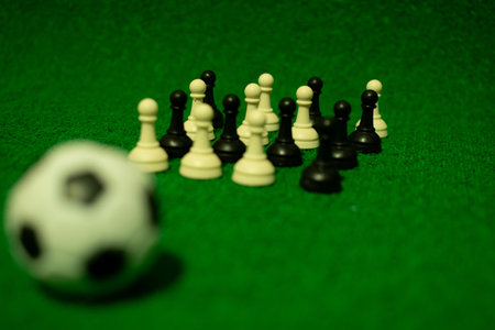 Black and white chess pieces on a green felt background with a soccer ballの写真素材