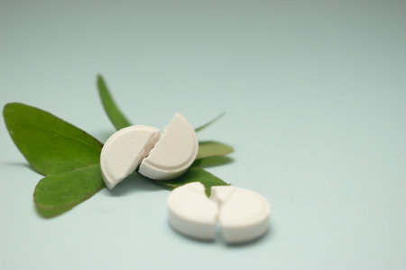 White pills with green leaves on blue background. Focus on foreground.