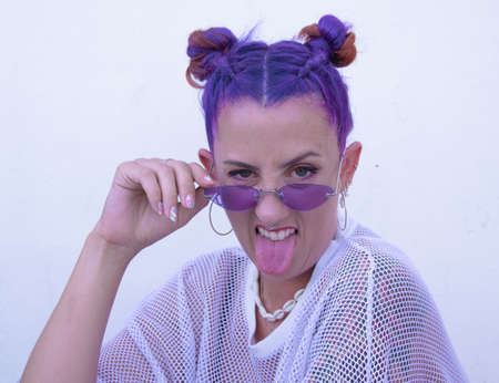 Purple stylish hair of a woman in a white background with her tongue outsideの写真素材