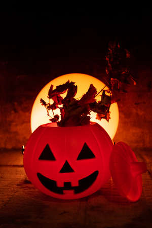 Creepy and terrifying halloween scene. Orange pumpkin, dry grass and a red moon or circular light behind in a stone backgroundの写真素材