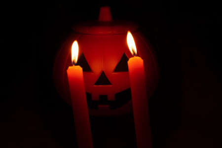 Halloween scene consisting of orange pumpkin with burning orange or red candles in the eyes. Red, orange and black lights.の写真素材