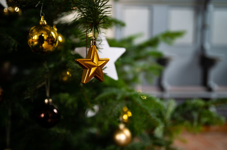 Yellow Gold Star Christmas Tree Ornament Handing on a Green Christmas Tree Branch with Blurred...