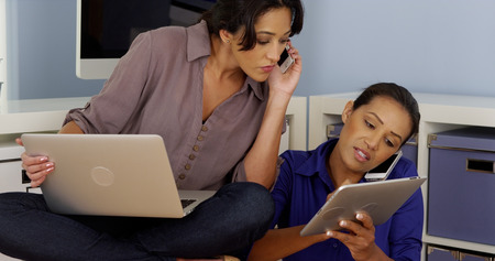 Black and Hispanic business women working together while talking on mobile phonesの写真素材