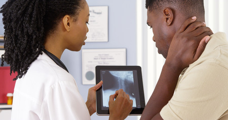 Patient with neck pain talking to female doctor about x ray on tabletの写真素材