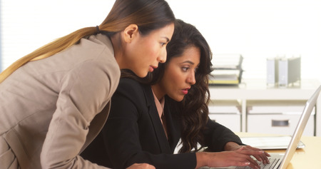 Mixed race business colleagues working at desk with laptopの写真素材