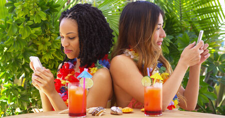 Black and Asian best friends on vacation using mobile phonesの写真素材