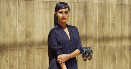 Black woman in dress leaning against wall and enjoying sun lightの写真素材