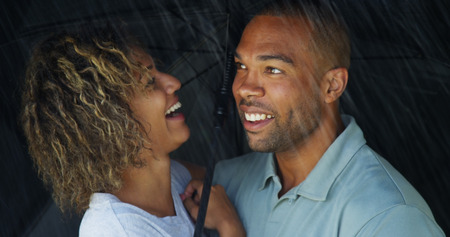 African couple laughing under umbrella togetherの写真素材