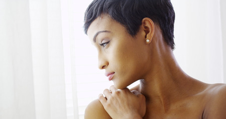 Beautiful topless black woman hugging herself and looking out windowの写真素材