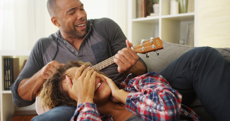 Happy black couple lying on couch with ukuleleの写真素材