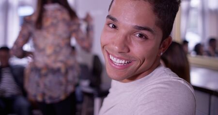 Portrait of Handsome young mixed race hipster man smiling at camera with group of friends partying in backgroundの写真素材