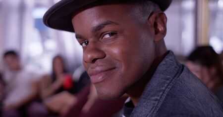 Portrait of Handsome young black hipster man smiling at camera with group of friends partying in...
