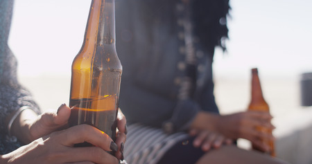 Close-up of woman holding beer bottle with friend in backgroundの写真素材