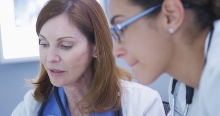 Tight shot of mid aged doctor talking with young assistant about patientの写真素材