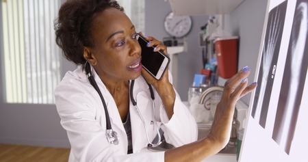 Portrait of African female doctor communicating on phone with colleague on xraysの写真素材