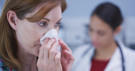 Attractive mid aaged patient blowing nose into tissue paper