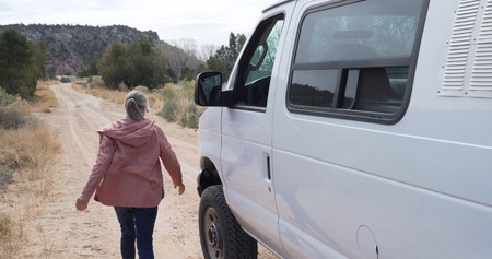 Candid senior woman in parked van stepping outside to walk away in natural parkの写真素材
