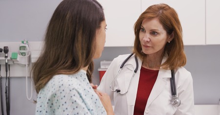 Professional female doctor attending to young latina patient in hospital gownの写真素材