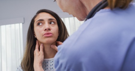 Senior nurse checking young patients neck for swollen lymph nodesの写真素材