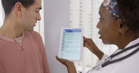 Senior African MD showing male latino patient different health plans on tabletの写真素材