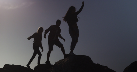Silhouette of friends walking on rocks at the beachの写真素材