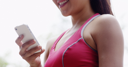 Young fit Asian woman resting texting at the parkの写真素材
