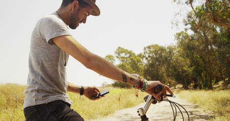 Sexy Hispanic man sitting on bike and using smartphoneの写真素材
