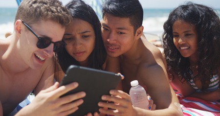 Healthy young interracial group of friends watching tablet at the beachの写真素材