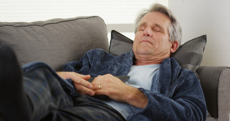 Mature man sleeping on a couch holding a tabletの写真素材