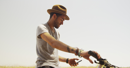 Sexy young man sitting on bike and using smartphone