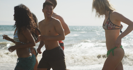 Happy Group of interracial friends running along beach shore waves laughingの写真素材