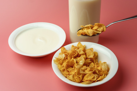 Corn flakes and yogurt in white bowl  with milk bottle place on pink background