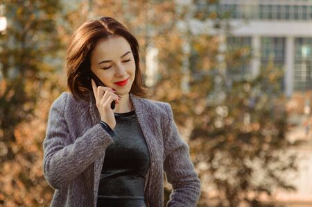 beautiful woman talking on the mobile phone in the autumn city parkの写真素材
