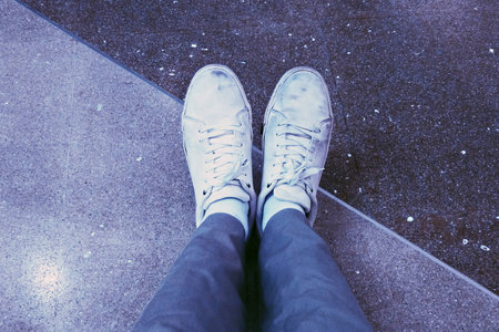 wearing dirty white sneakers with two tone granite floor in the backgroundの写真素材